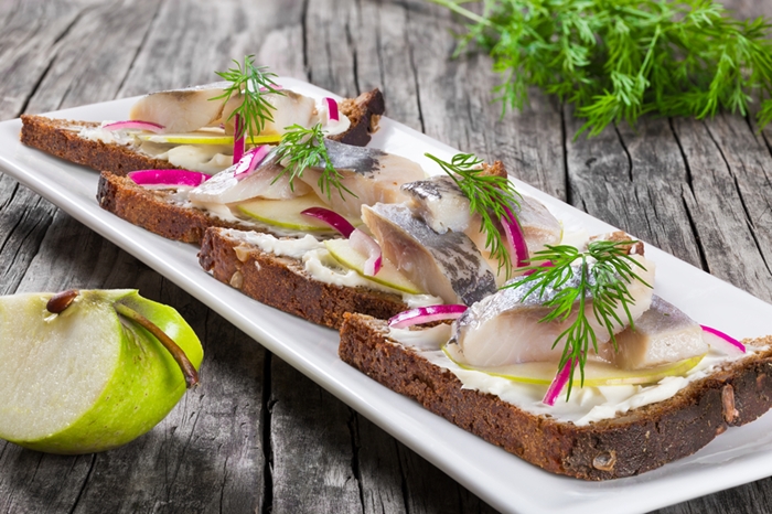 sandwich with herring fillets, onion, pickled cucumber and dill on parchment paper on an oval dish on an old rustic table, traditional street food in Norway, close-up
