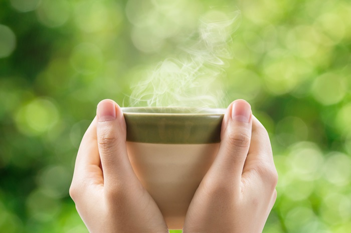 Hands holding tea cup on green bokeh background.