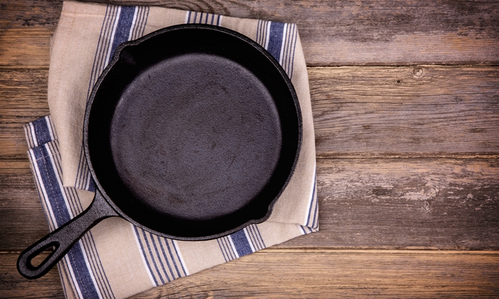 Empty cast iron skillet with tea towel, over old wood background. Retro style processing and space for your text.